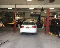 A white sedan parked inside an auto repair shop with multiple service bays and car lifts.