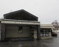 Exterior of Hudson View Auto Body Inc., featuring a tan building with a large peaked entryway and glass-fronted office.