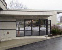 A ground-level view of a commercial building entrance with a concrete wheelchair ramp leading to a glass double door.