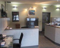 A well-lit administrative office interior with reception desks, a black office chair, and wall-mounted artwork.