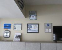 Wall-mounted framed certificates and advertisements, including a small monitor and a television, displayed in an office.