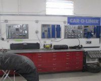 A bright auto body shop workspace featuring a long red workbench with tool boards and Car-O-Liner signage on the wall.