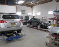 An auto repair shop interior featuring a silver SUV on a lift and a black sedan parked on a frame rack.