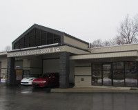 Exterior view of Hudson View Auto Body Inc. with a red car parked under the building overhang on a gray, overcast day.