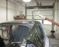 An auto body frame machine pulling a dent on the roof of a gray car inside a workshop.