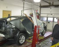 A mechanic uses a red frame machine to align the body of a dark car in a garage.