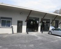 Light-colored automotive repair shop exterior with open service bays and a silver car parked in front.