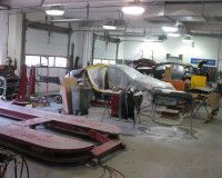 An auto body shop with a car under a protective cover, a red frame machine in the foreground, and tools in a workspace.