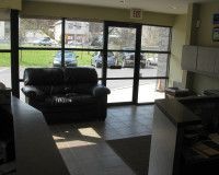 A waiting area with a dark leather sofa in front of large windows showing a parking lot.