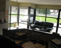 A reception desk in an office with a black leather sofa near large windows overlooking a parking area.