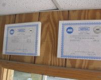 Two framed ASE professional automotive service certificates hanging on a wood-paneled wall.
