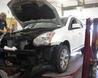 A mechanic works on the engine of a white SUV with its hood open in an auto repair shop.