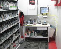 A mixing room with shelves of paint cans next to a workstation featuring a computer, monitor, and scale.