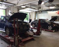 Two cars with open hoods parked on red automotive lifts inside a well-lit repair shop.