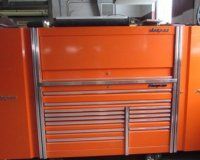 A bright orange Snap-on roll cabinet with multiple metal drawers and chrome trim in a workshop setting.