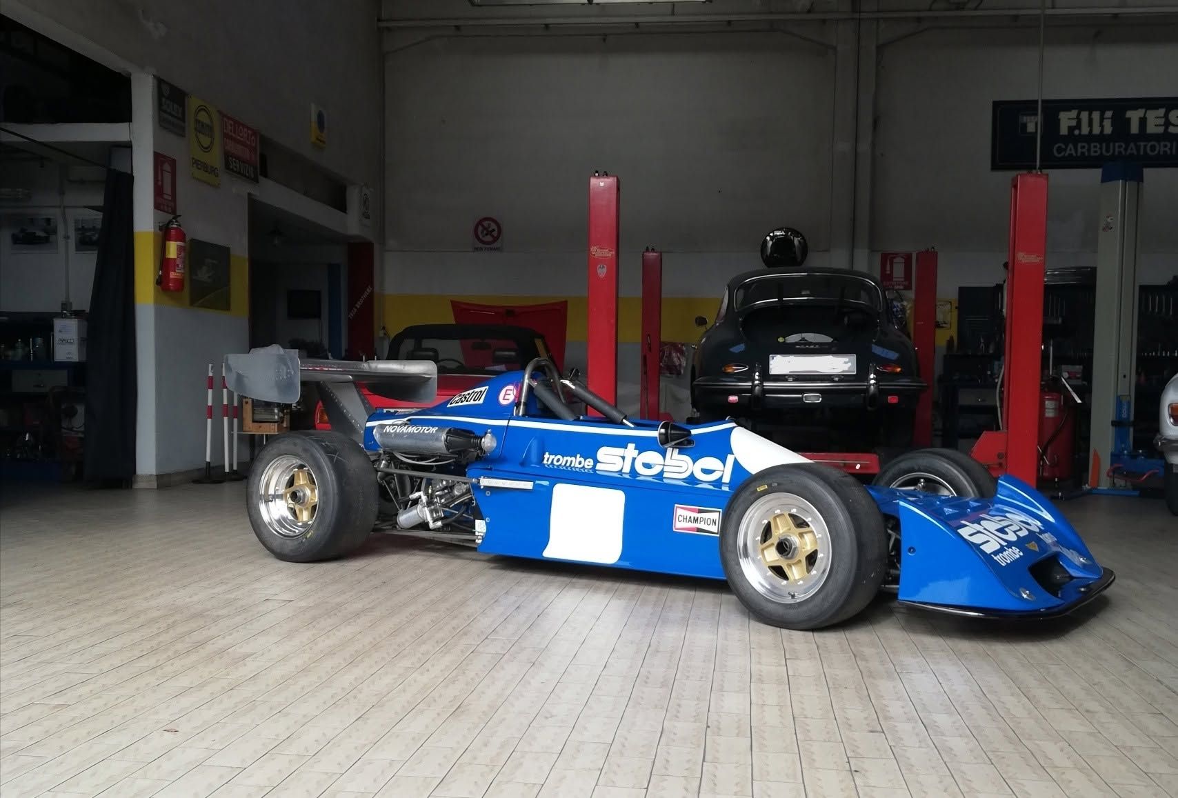 Una monoposto di Formula blu parcheggiata in un garage, con un'altra auto sullo sfondo.