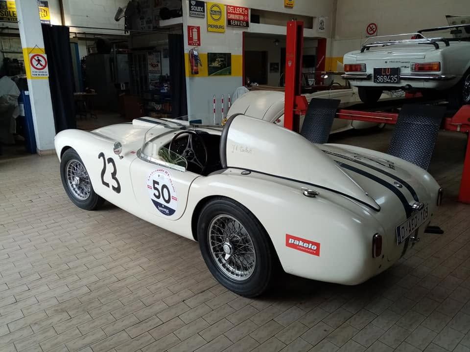Auto da corsa d'epoca bianca con il numero 23 parcheggiata in un garage, con il cofano motore posteriore aperto.