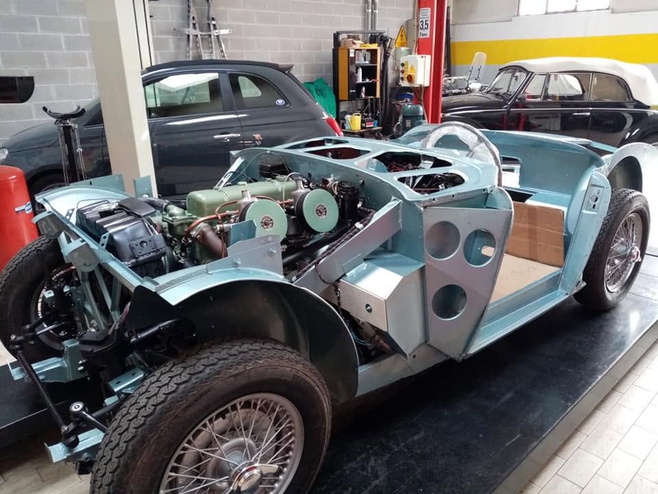 Auto sportiva d'epoca parzialmente restaurata in un garage, con motore a vista e pannelli della carrozzeria color verde acqua.