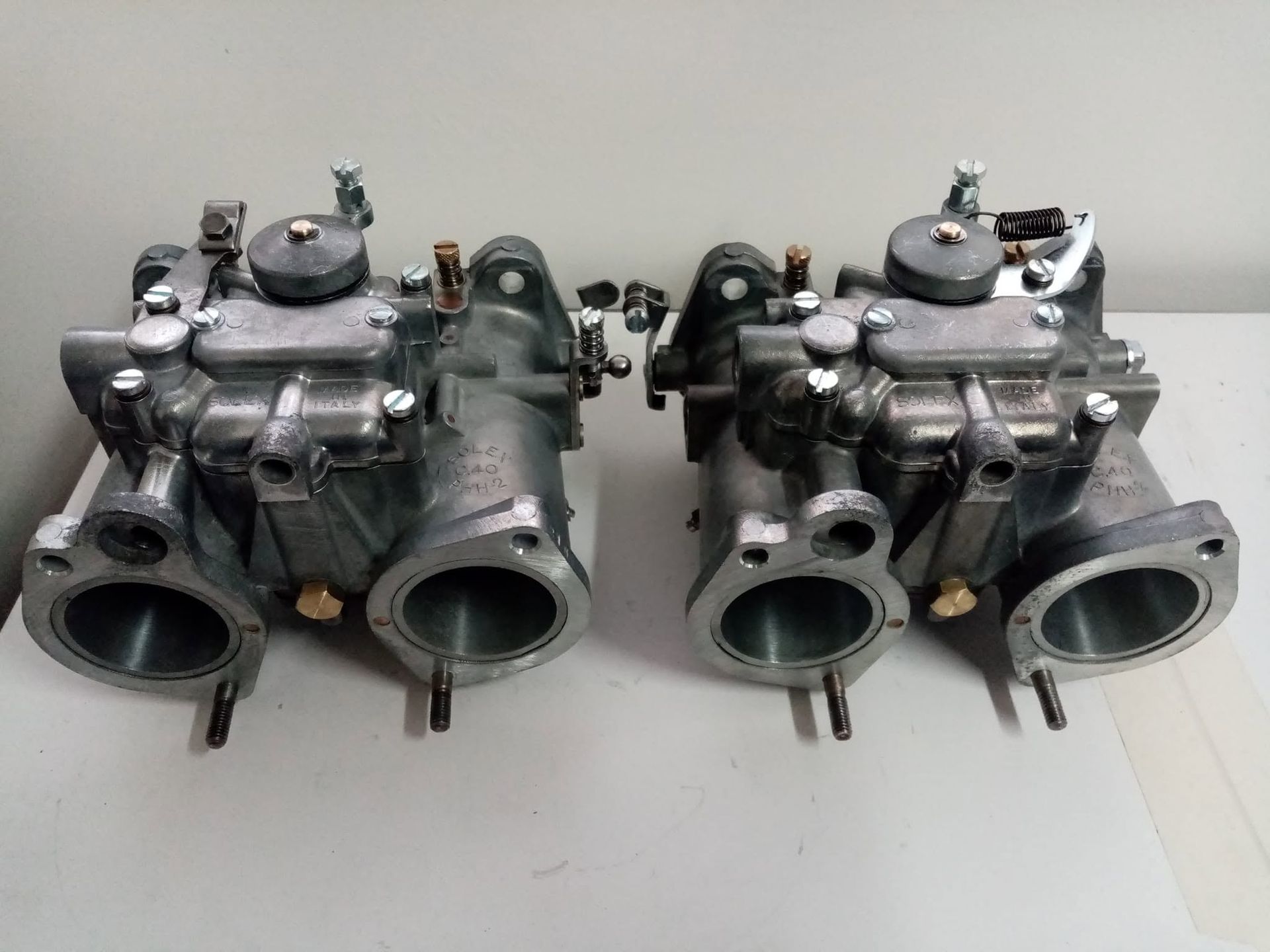 Due carburatori argentati affiancati su una superficie grigio chiaro