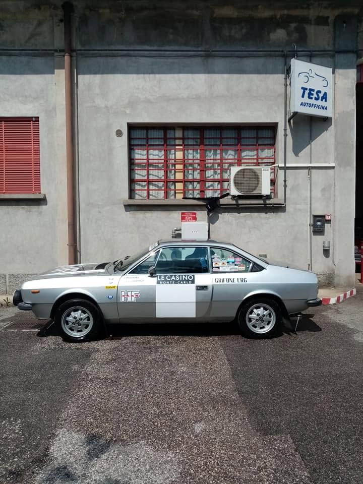 Un taxi argentato parcheggiato accanto a un edificio grigio con una finestra rossa e un condizionatore d'aria.