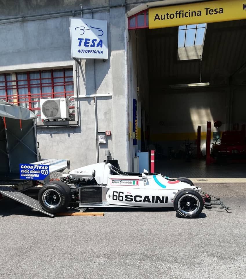 Auto da corsa parcheggiata fuori dal garage dell'officina Tesa, con livrea Scania bianca e tettuccio giallo.