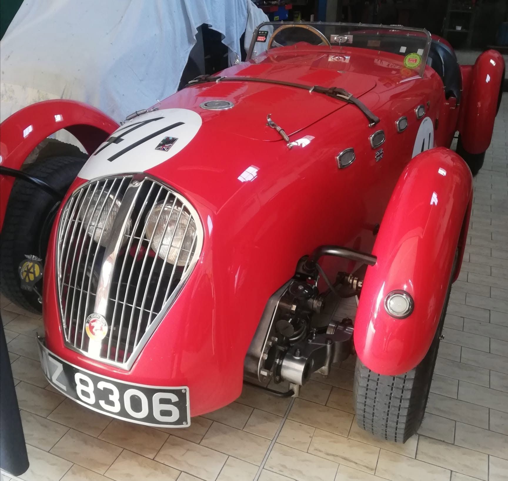 Auto da corsa d'epoca rossa con numero 4 bianco e targa 8306, esposta in interni.