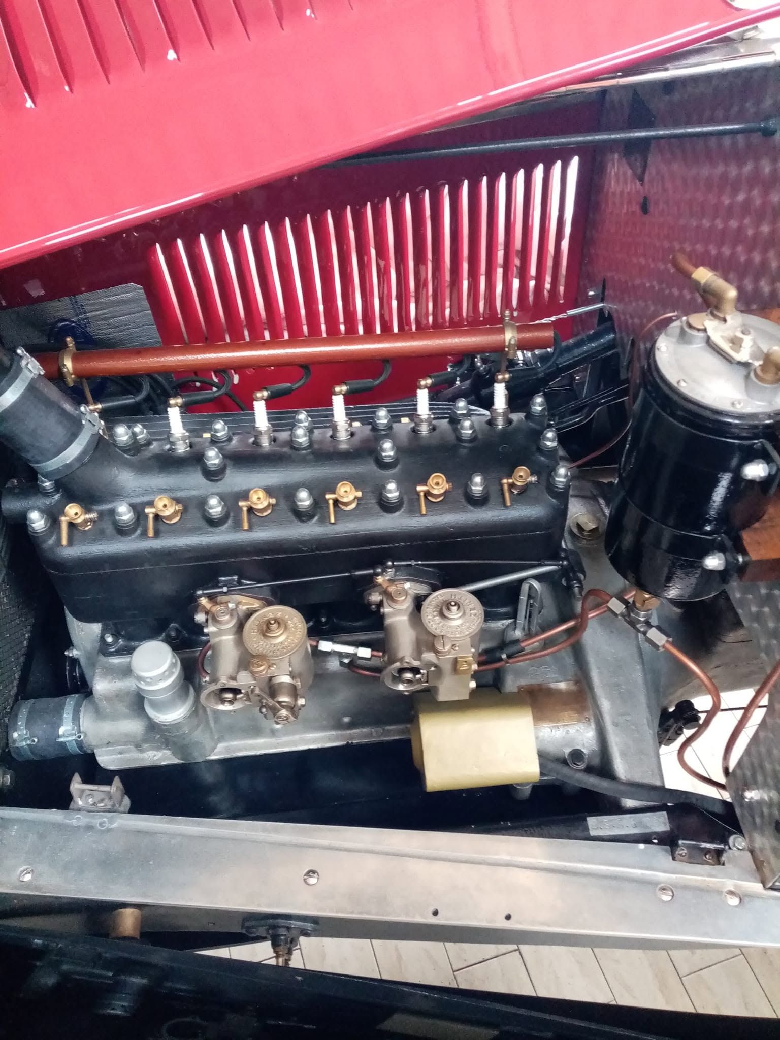 Primo piano del vano motore di un'auto d'epoca con componenti neri e rivestimento del cofano rosso.