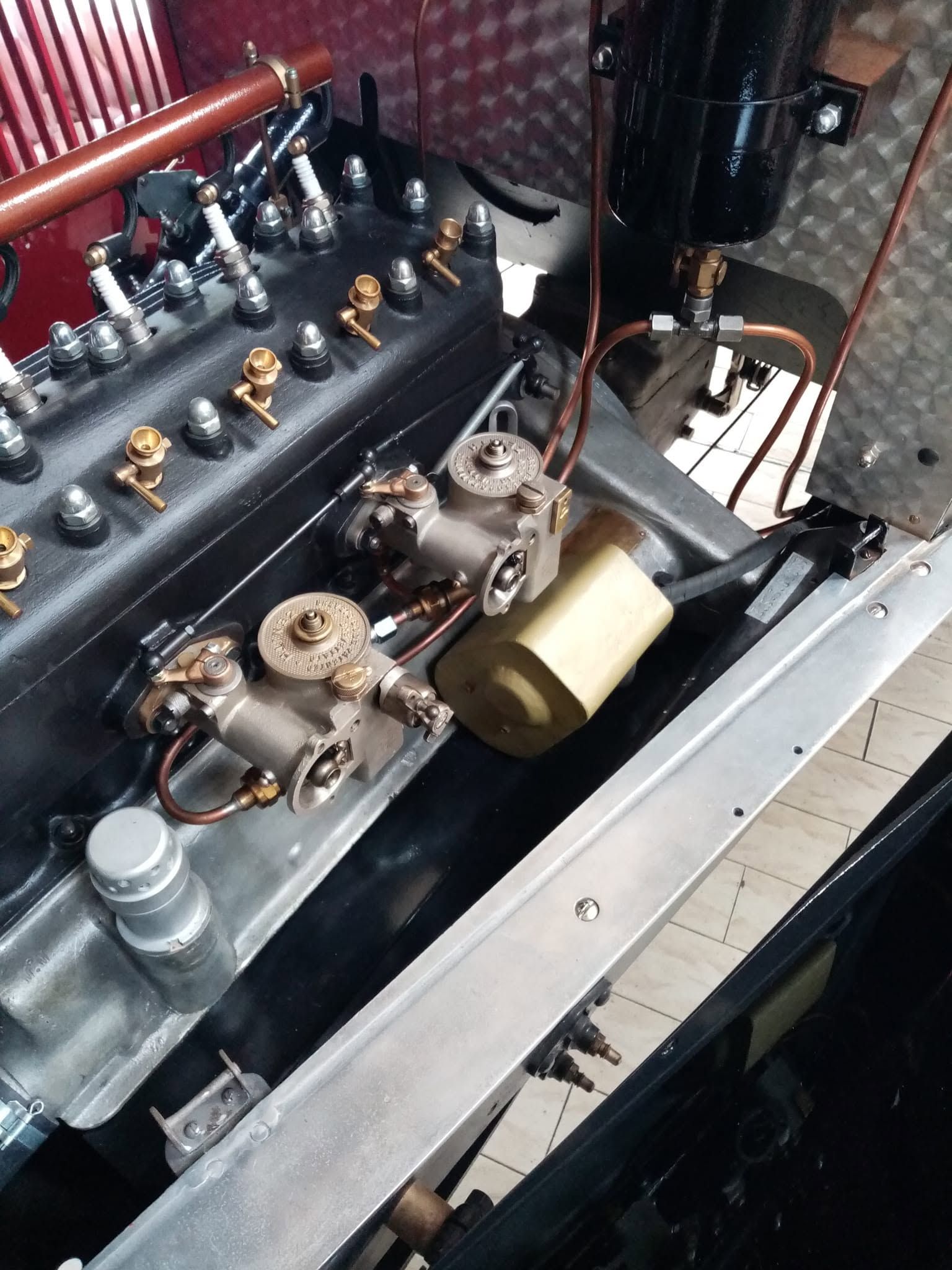 Primo piano di un motore meccanico d'epoca con componenti in ottone e metallo all'interno di un vano motore.