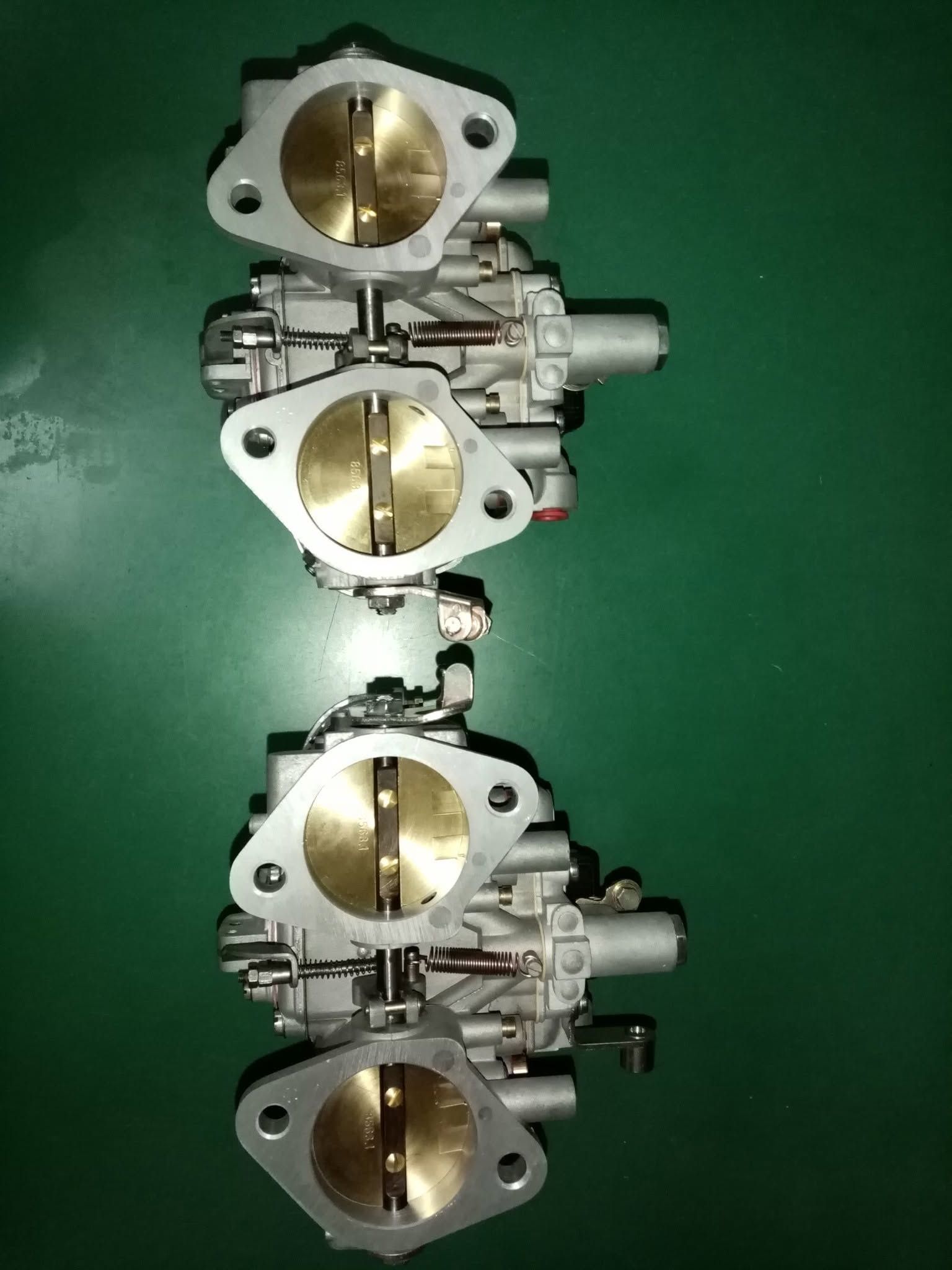 Tre corpi farfallati metallici con valvole in ottone impilati verticalmente su uno sfondo verde