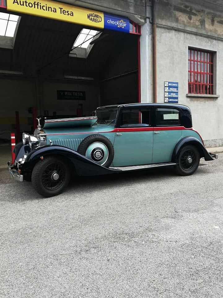 Auto d'epoca nera e turchese parcheggiata fuori dal garage di un'officina.