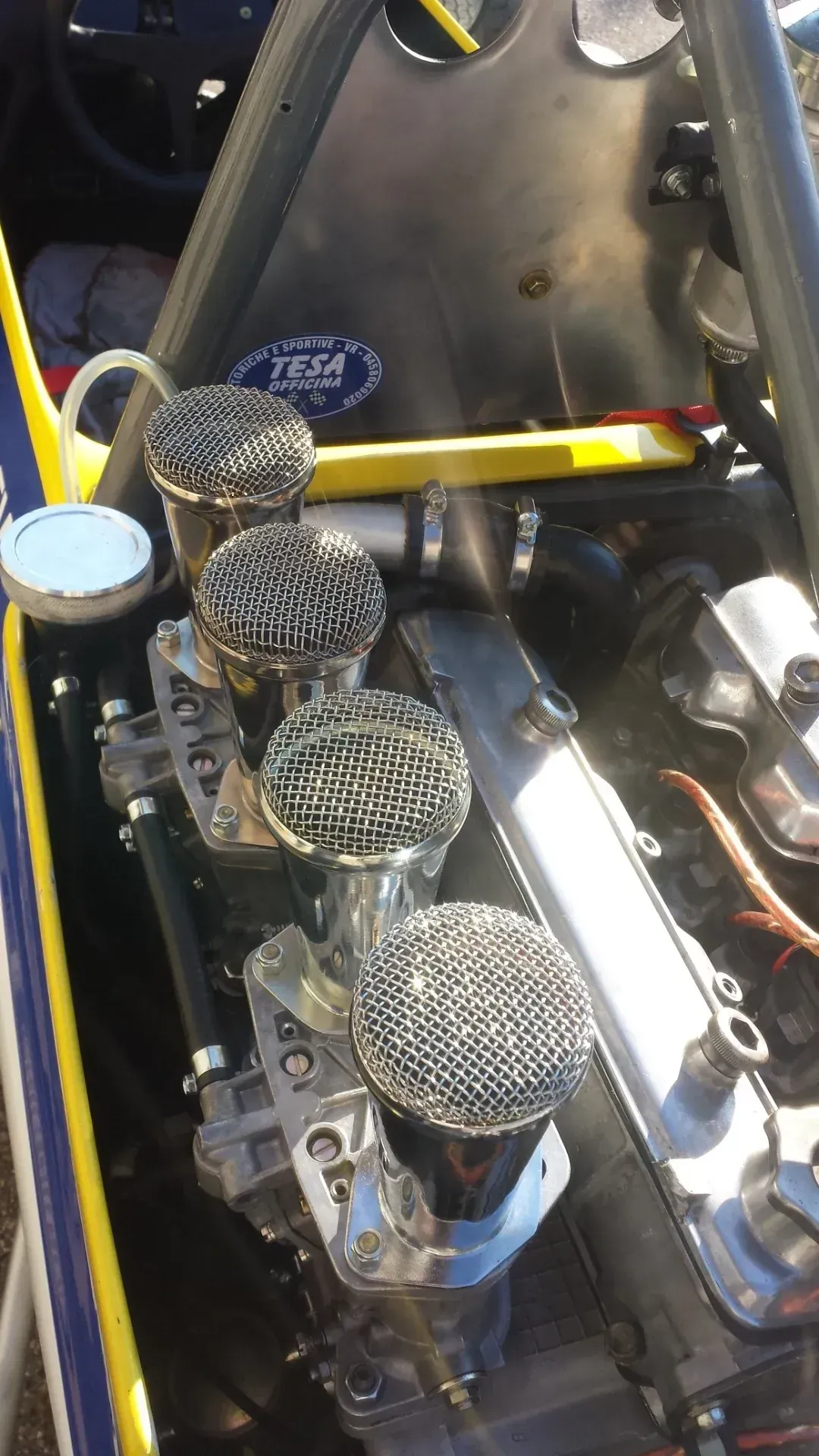 Primo piano di un motore di motocicletta con quattro filtri dell'aria rotondi e componenti metallici.
