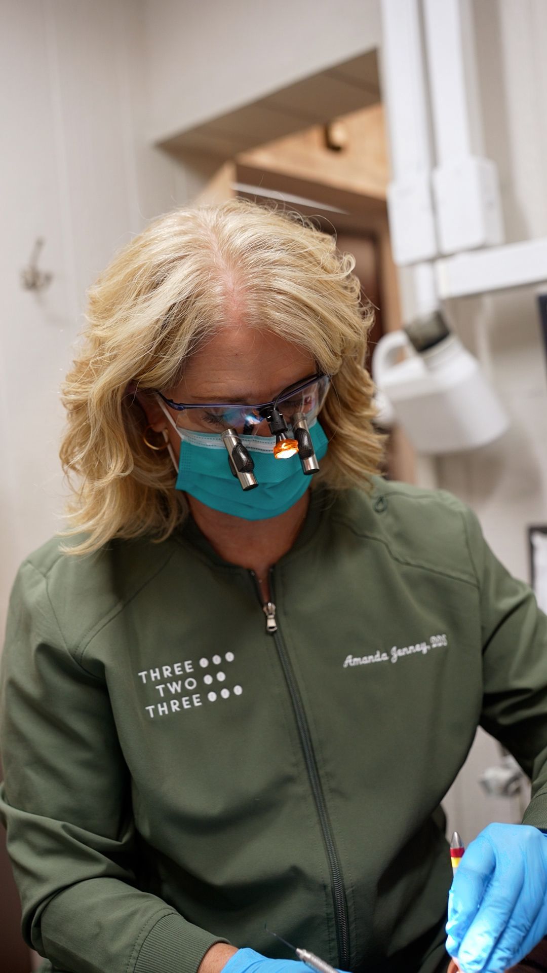 Dentist in green scrubs and mask, looking down while working in a clinical setting
