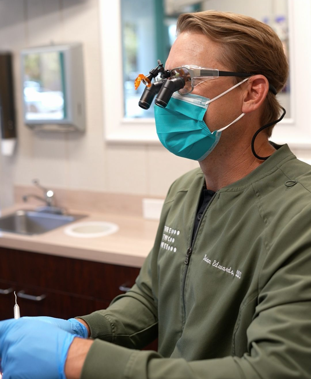 Dentist wearing mask and magnifying loupes, preparing for a dental procedure in a clinic