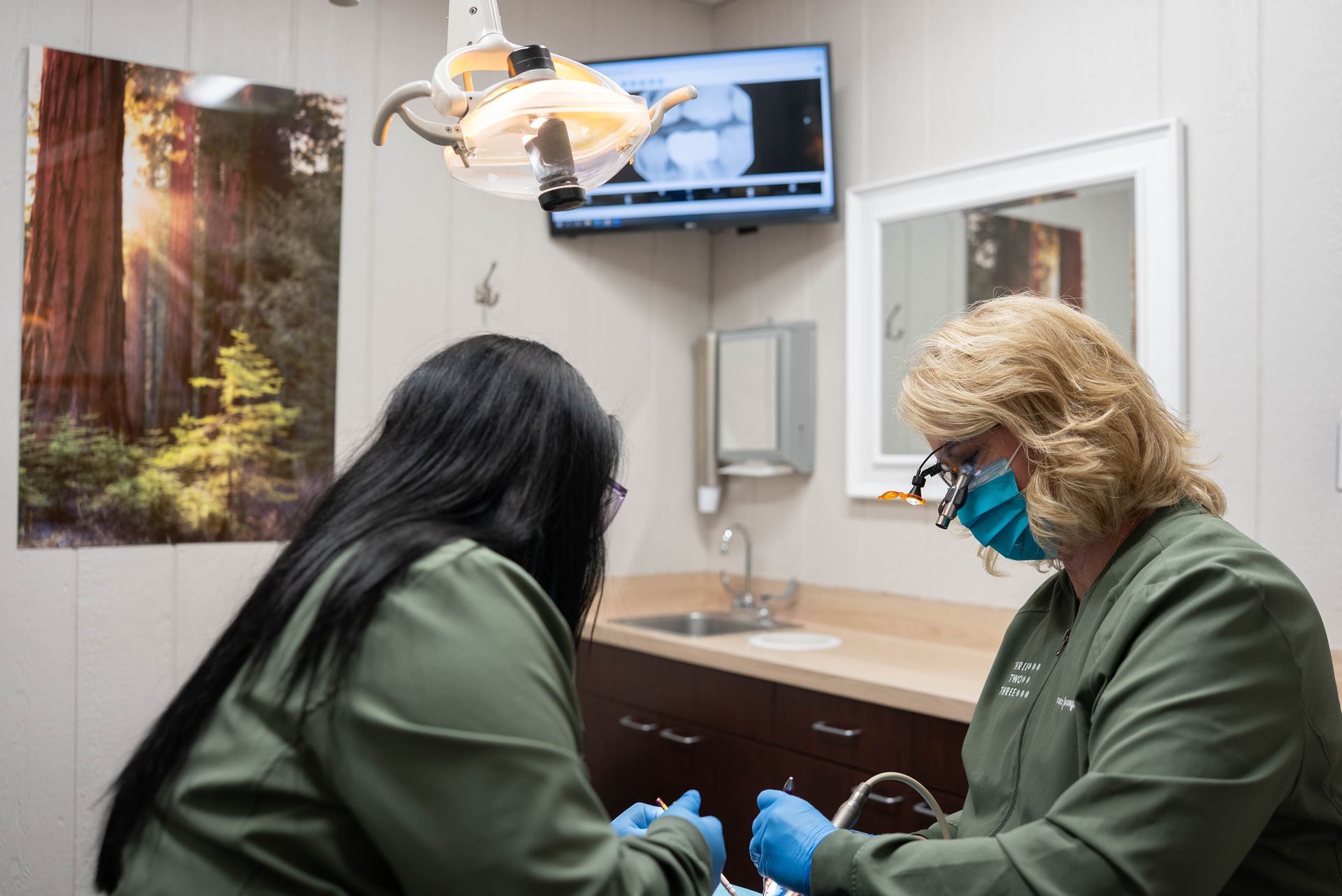 Dental exam with two clinicians in green scrubs treating a patient in a bright, modern office