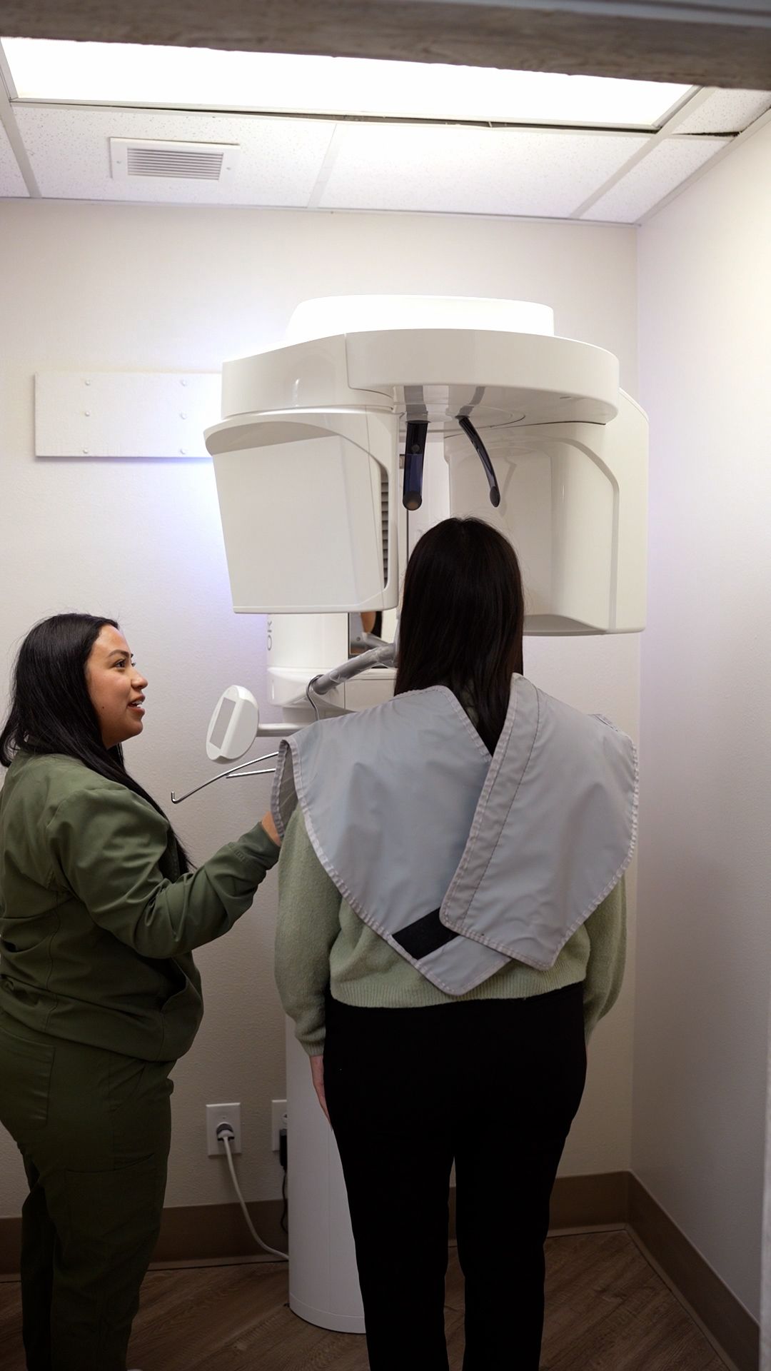 Two people adjusting a medical imaging machine in a small exam room