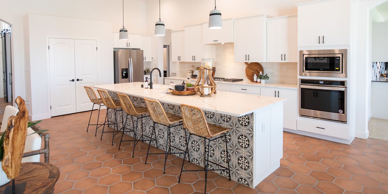 A modern kitchen with a large island, white cabinets, and woven bar stools.