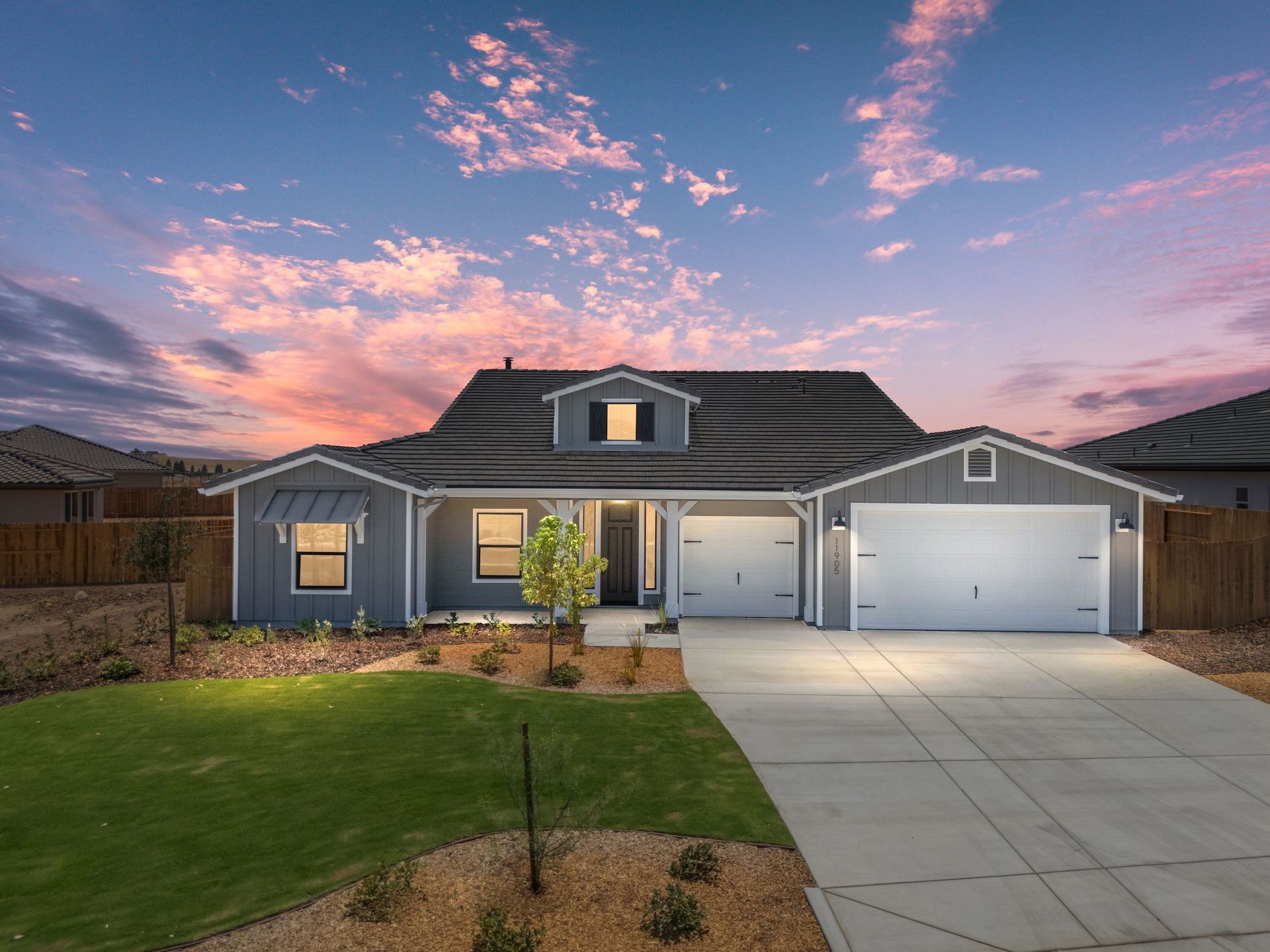 Gray house with a two-car garage, manicured lawn, and driveway; sunset sky.