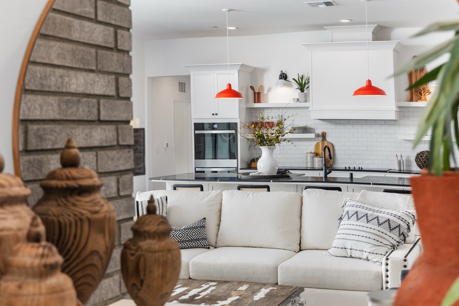 Modern kitchen and living room: white cabinets, red pendant lights, white sofa, brick column.