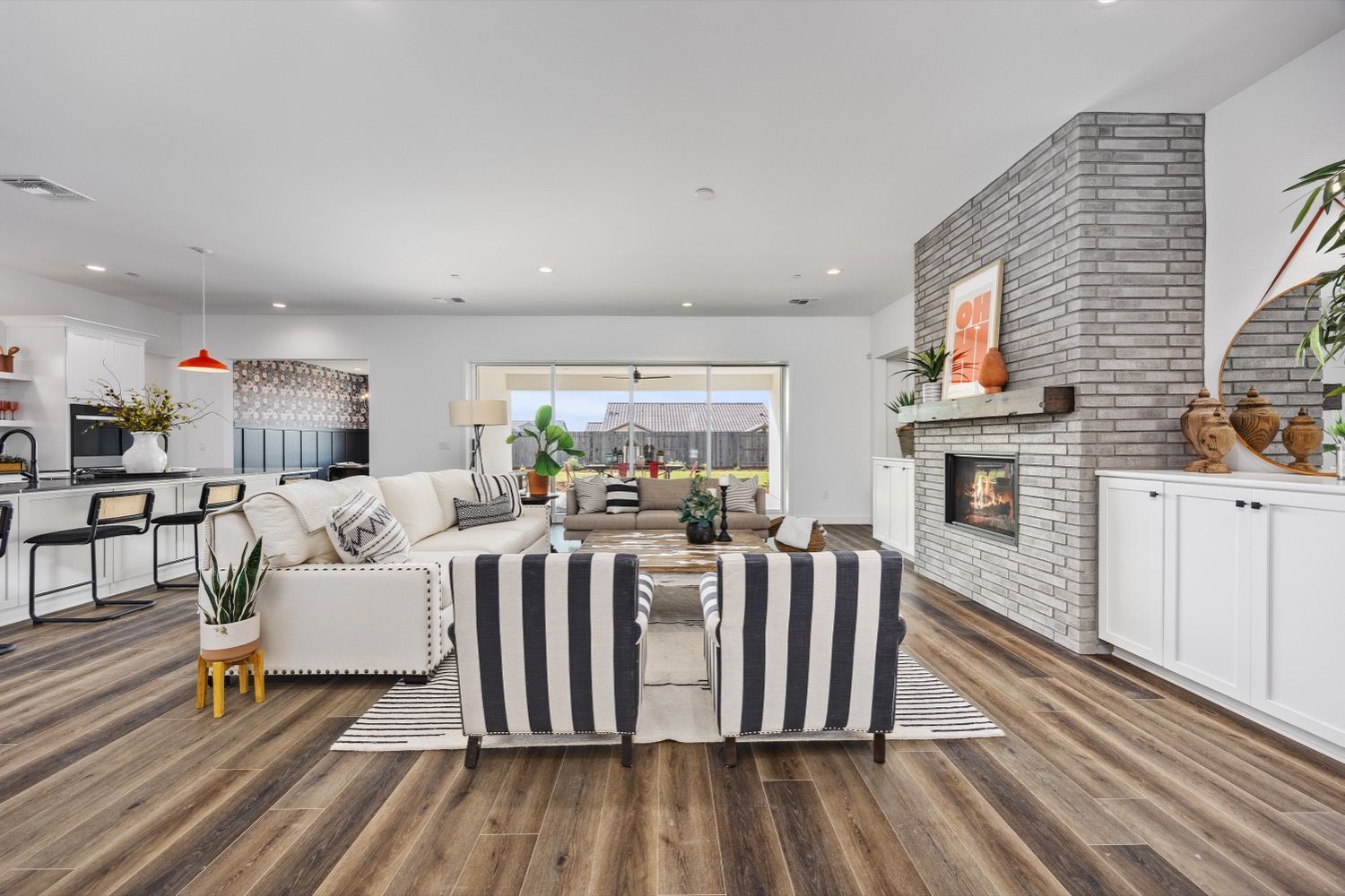 Spacious modern living room with fireplace, white walls, and wood-look flooring. Black and white striped chairs face fireplace.