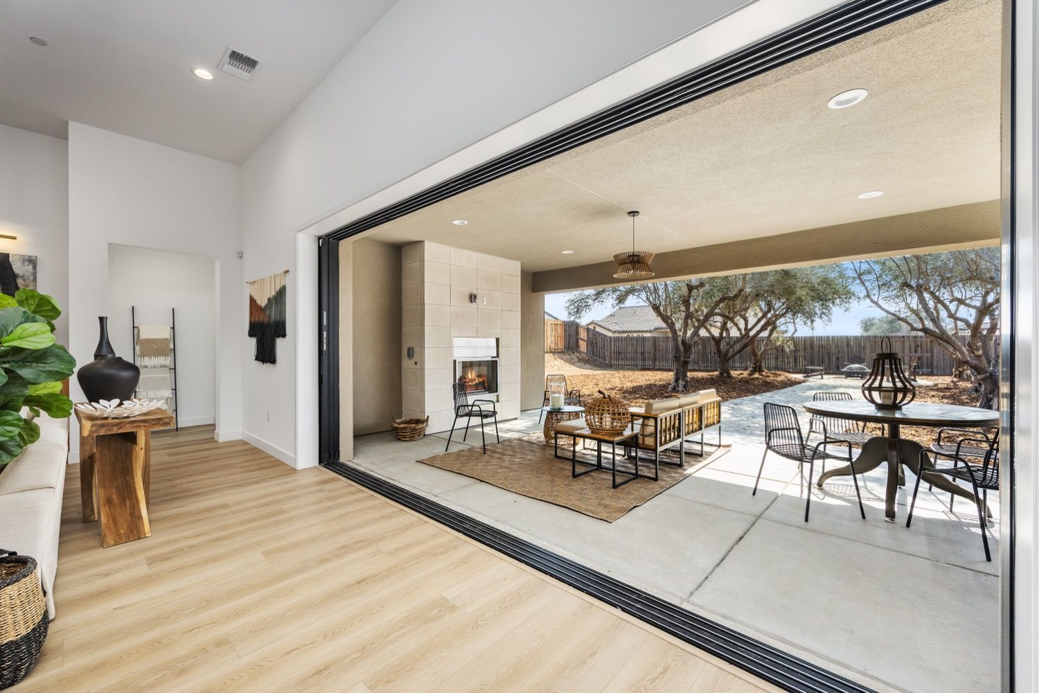 Open-plan living space with indoor and outdoor areas; light wood floors, large sliding doors, patio furniture.