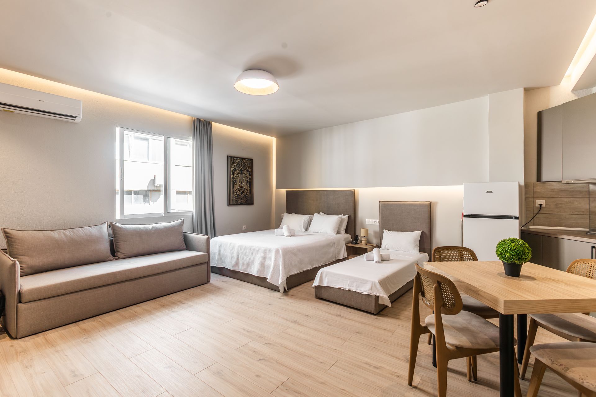 Studio apartment with a bed, sofa, dining table, and small kitchen. Natural light.