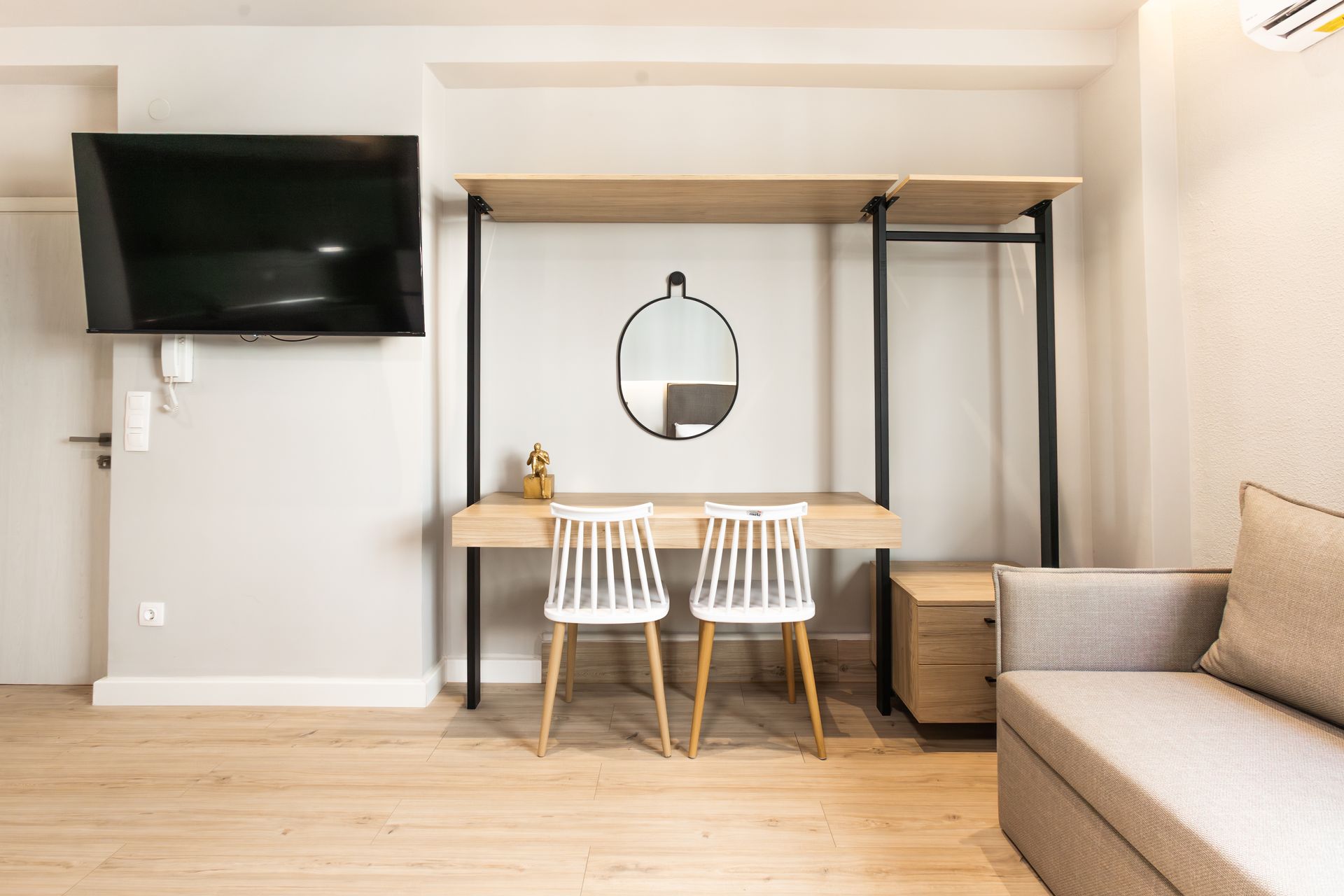 Modern room with desk, chairs, TV, and couch.  Neutral colors and minimalist design.