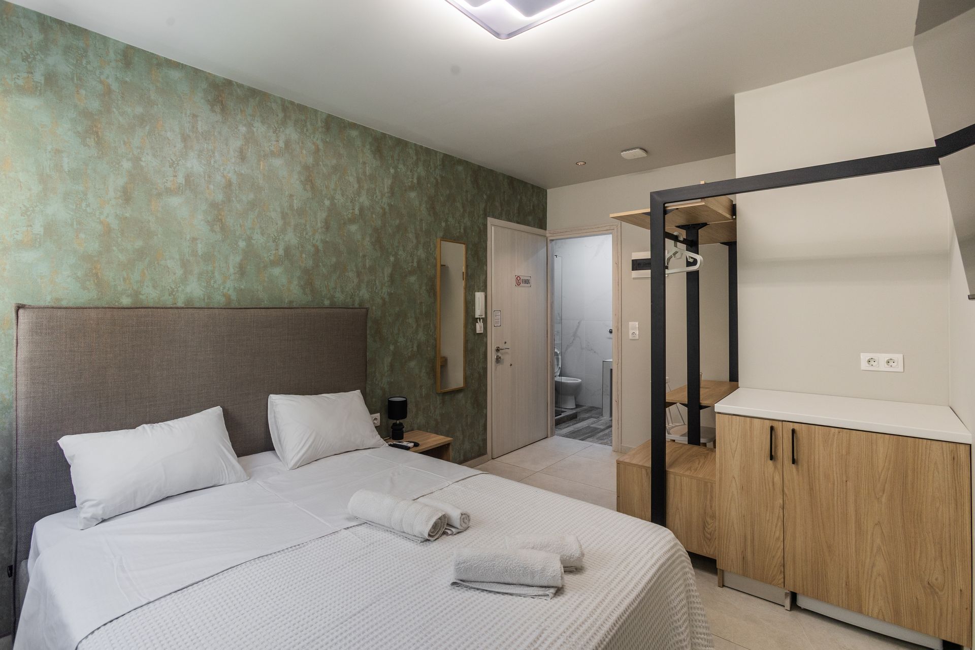 Bedroom with queen bed, green textured wall, open closet, and a glimpse of the bathroom.