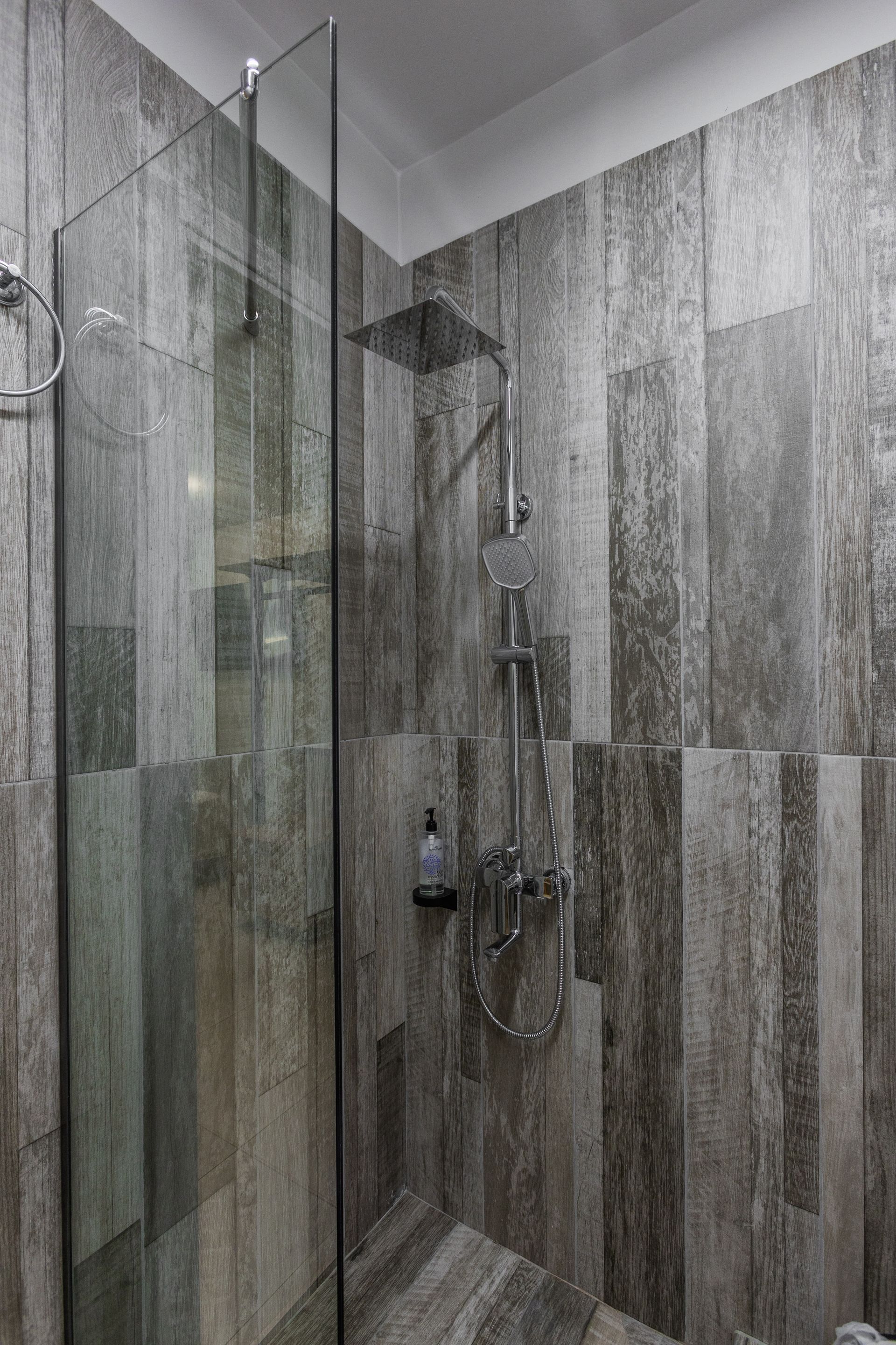 Shower with glass door, gray wooden-look tile walls, and a silver shower head and fixtures.