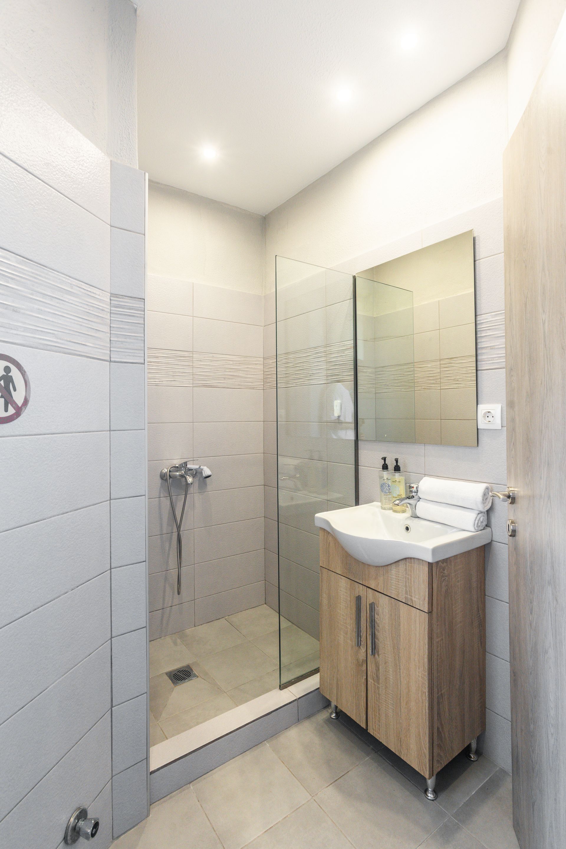 Small bathroom with glass shower, sink, wooden cabinet, and large mirror.
