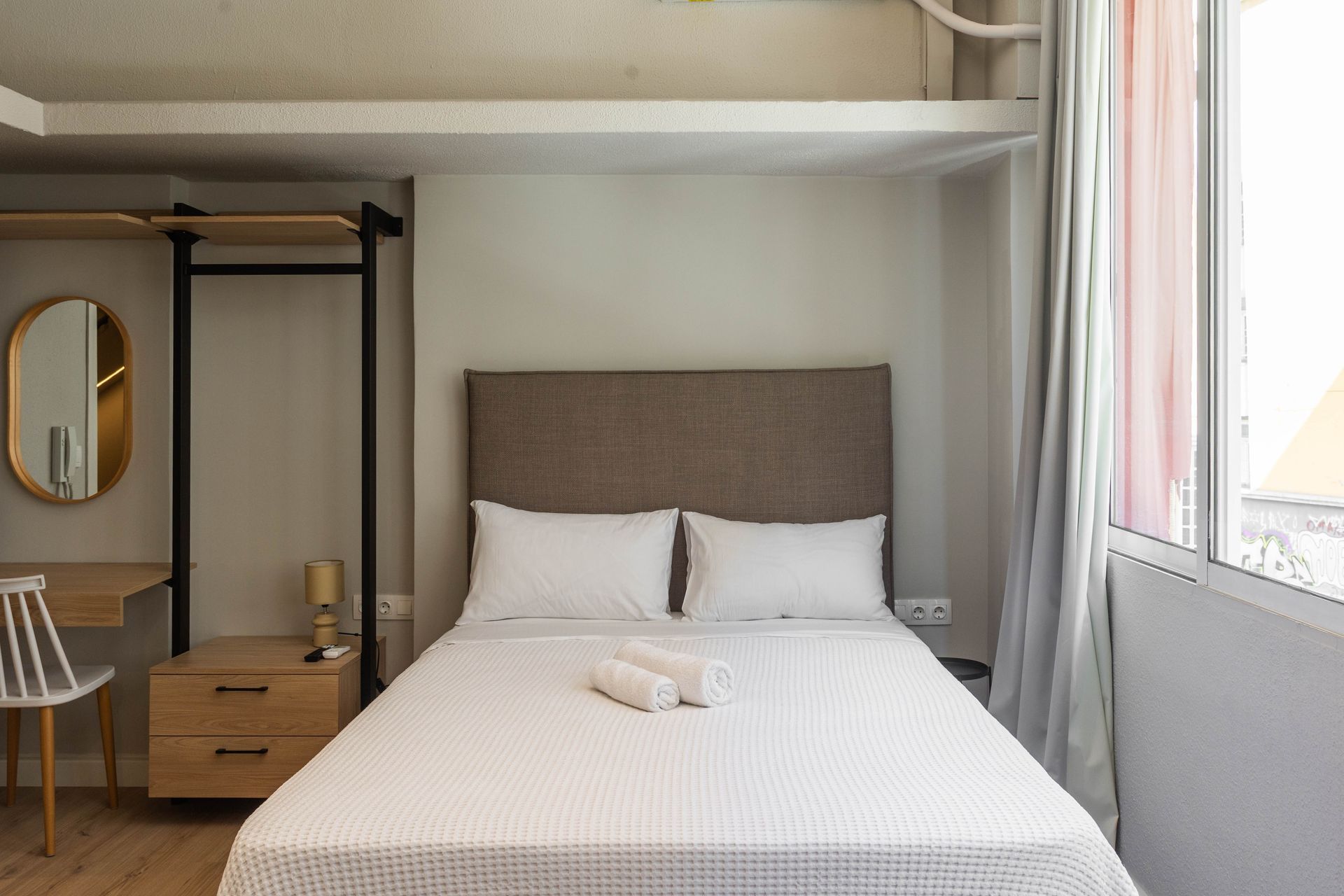 Cozy, modern bedroom with a double bed, dresser, desk, and window with curtains.