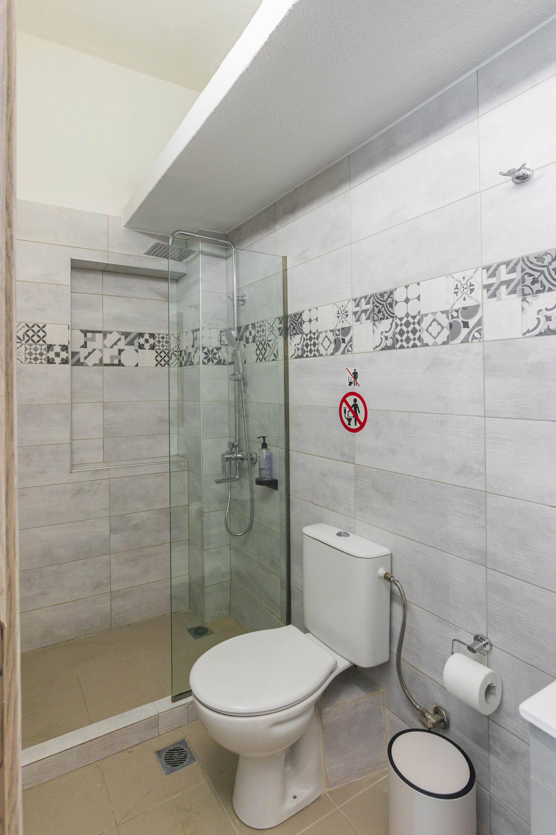 Bathroom with a toilet, shower, and patterned tile walls.