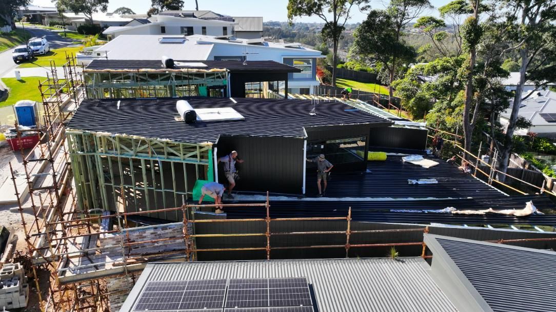 Man is Kneeling on the Top of a Roof Measuring a Piece of Metal — Roofing Contractor in Wauchope, NSW