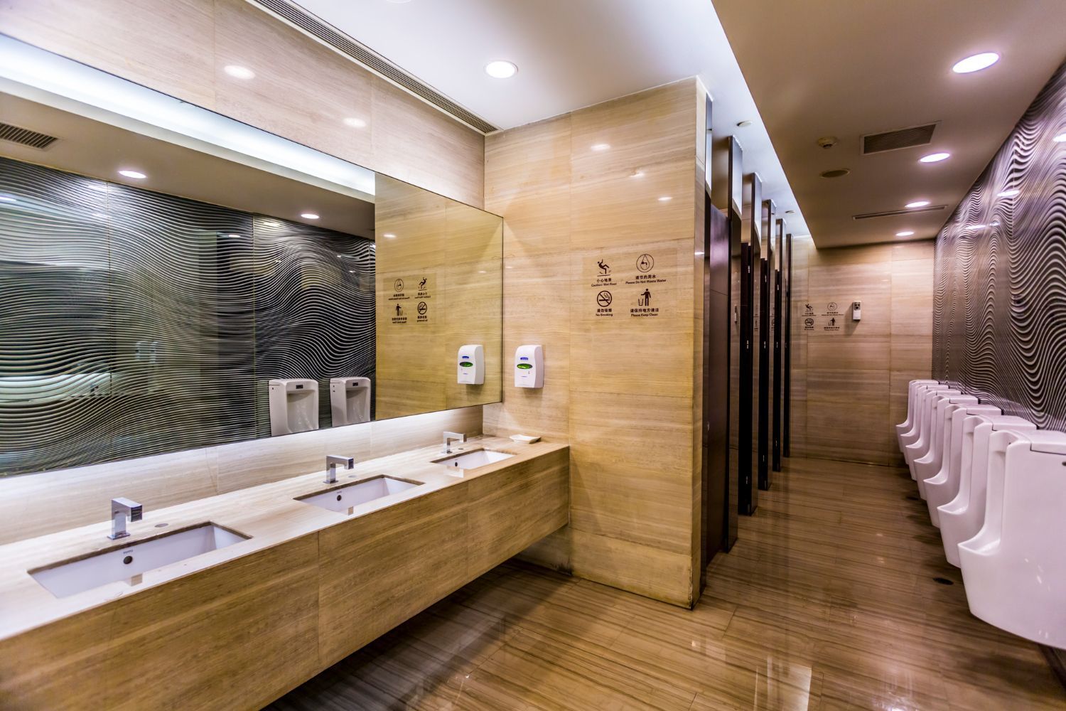 Modern public restroom with wood-paneled walls, long sink counter, mirrors, and rows of urinals.