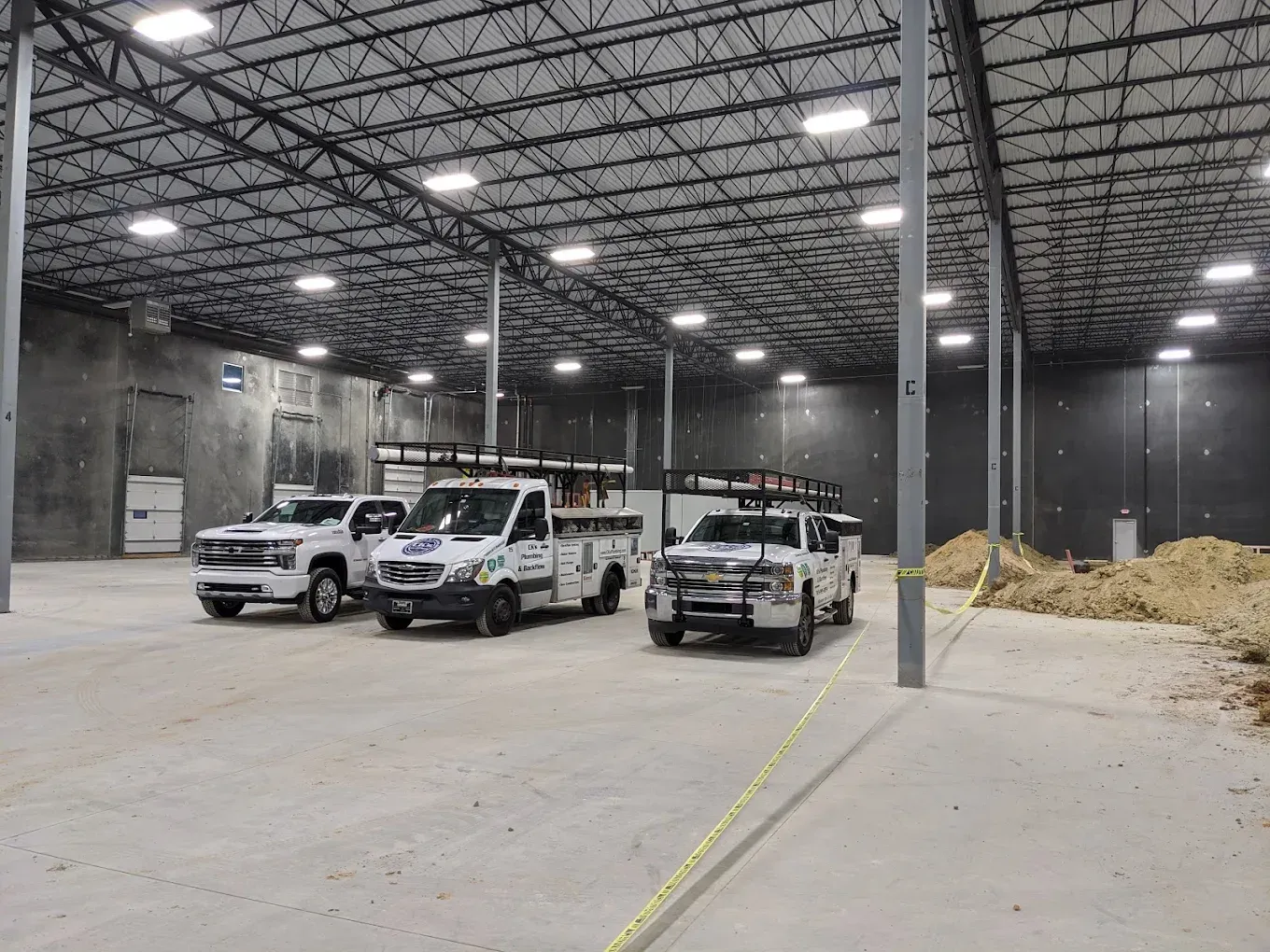 Construction warehouse interior with three white pickup trucks parked on a concrete floor.